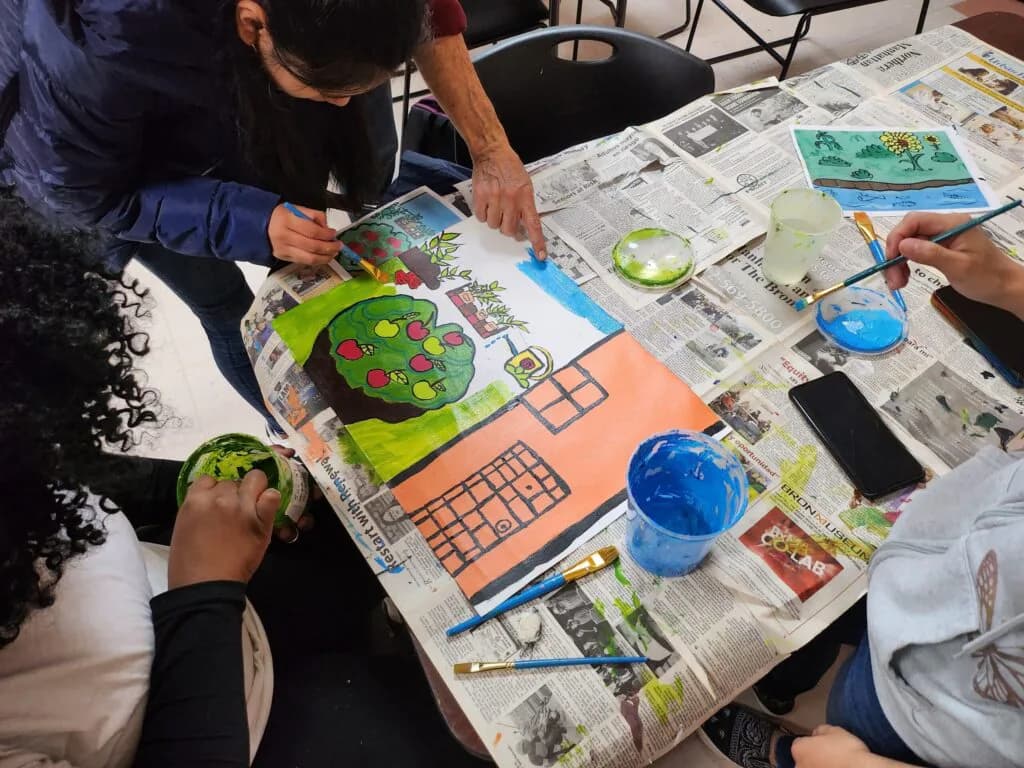 Children's hands engaged in a painting or craft activity on newspaper-covered table with colorful circular artwork and blue containers.